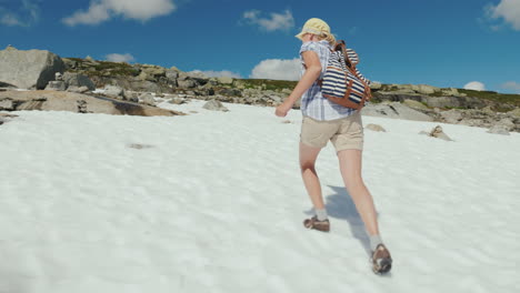 a woman is walking on the snow in the mountains outside it's a hot summer the snow has not melted ye