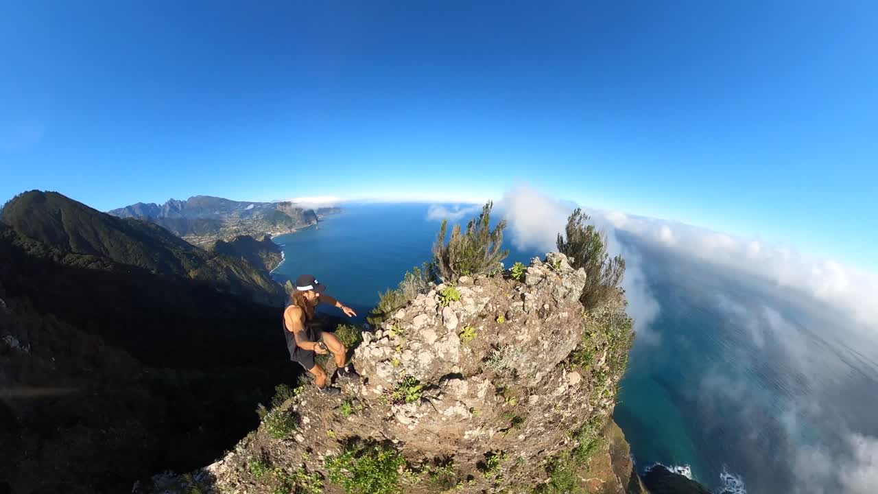 un excursionista solitario joven y fuerte camina por el borde empinado de espigao amelo en madeira con una cámara de acción de 360 grados en un palo selfie con una vista increíble del paisaje y el océano debajo de él