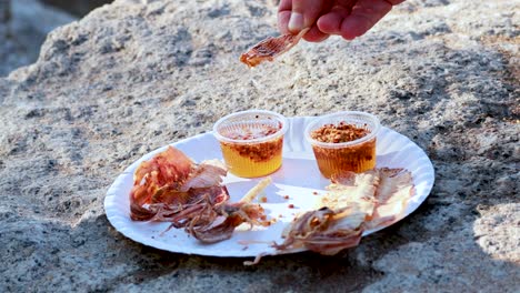 hand holding dried seafood snack with dipping sauce on a rock