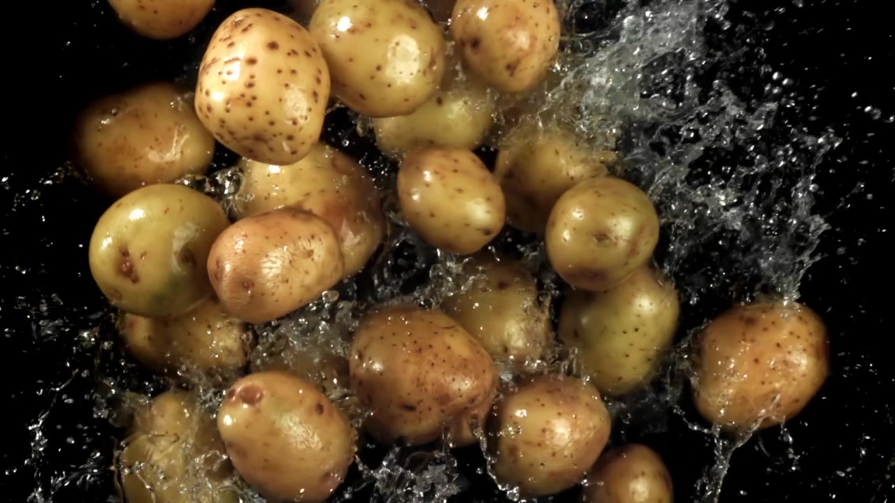 Patate fresche che cadono e schizzano nell'acqua su sfondo nero