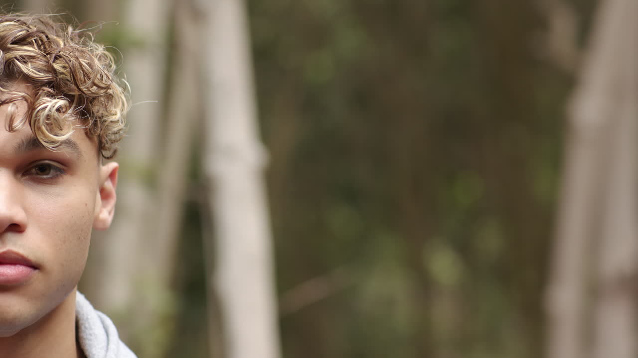 Young man with curly hair standing outdoors, looking thoughtful in nature, copy space