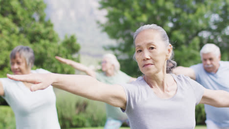 Sonriente-Mujer-Asiática-Mayor-Practicando-Yoga-Con-Un-Grupo-Diverso-De-Personas-Mayores-En-El-Jardín,-Cámara-Lenta