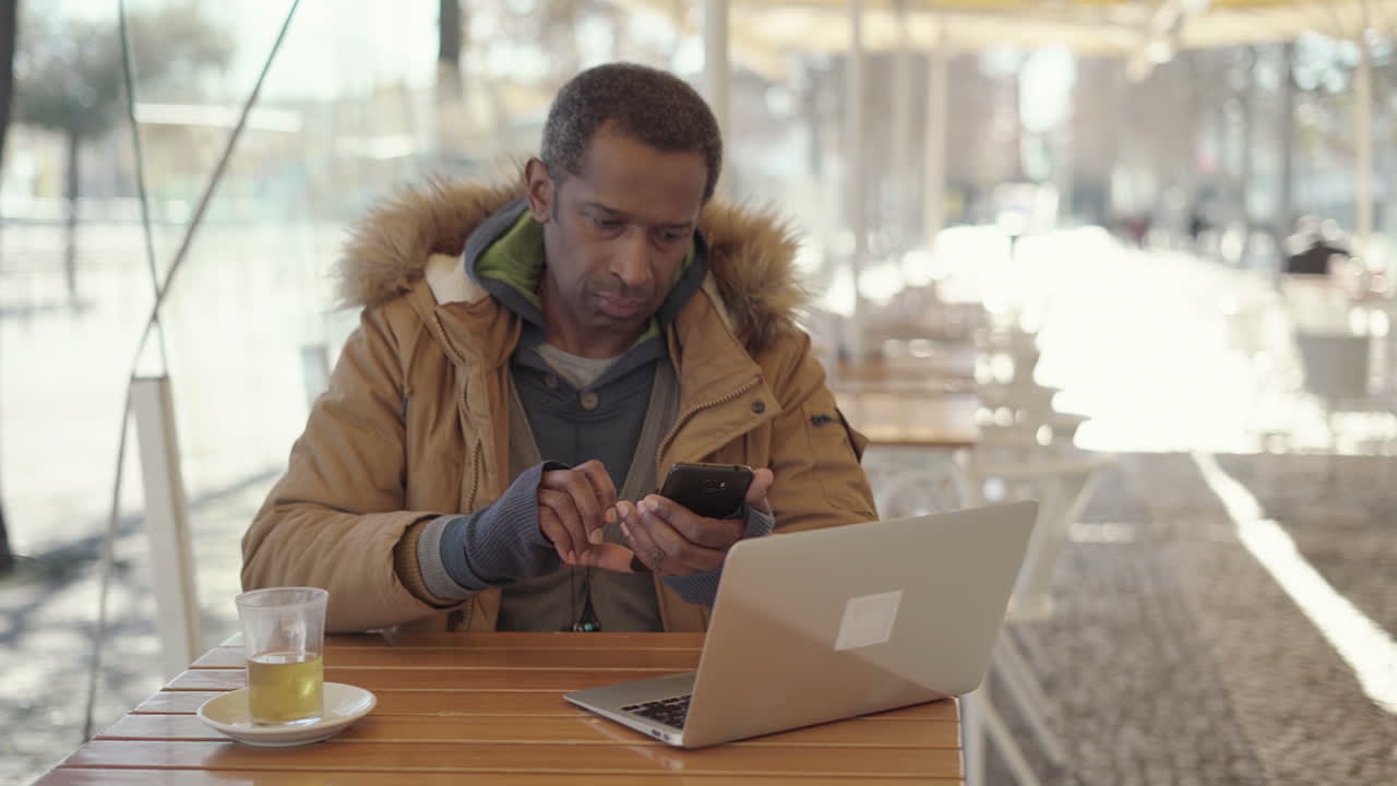 African American man using laptop and cell phone in cafe