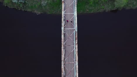 couple walking on pedestrian bridge over river gauja in latvia, top down view