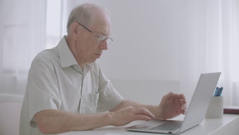 hombre anciano está trabajando de forma remota escribiendo y enviando mensajes por correo electrónico usando internet en una computadora portátil quedándose en casa
