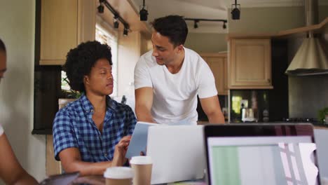 two diverse male friends in kitchen and working on laptop
