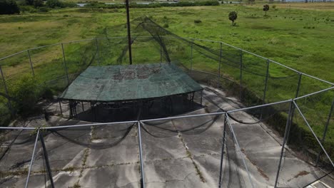 aerial-of-an-abandoned-amusement-batting-practice-cage,-dramatic-flight-by-old-lighting-post