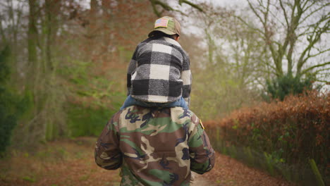 vista trasera de un soldado en uniforme que regresa a casa con su familia en licencia llevando a su hijo con una gorra militar