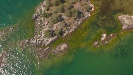 Drone-Volando-Hacia-Arriba-Y-Lejos-De-Una-Pequeña-Isla-Con-Verde-Ver-A-Través-Del-Mar-De-Agua