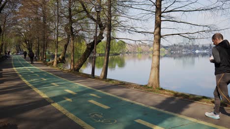 Grupo-De-Personas-No-Identificadas-Trotando-En-El-Parque-Con-Lago-Durante-El-Día