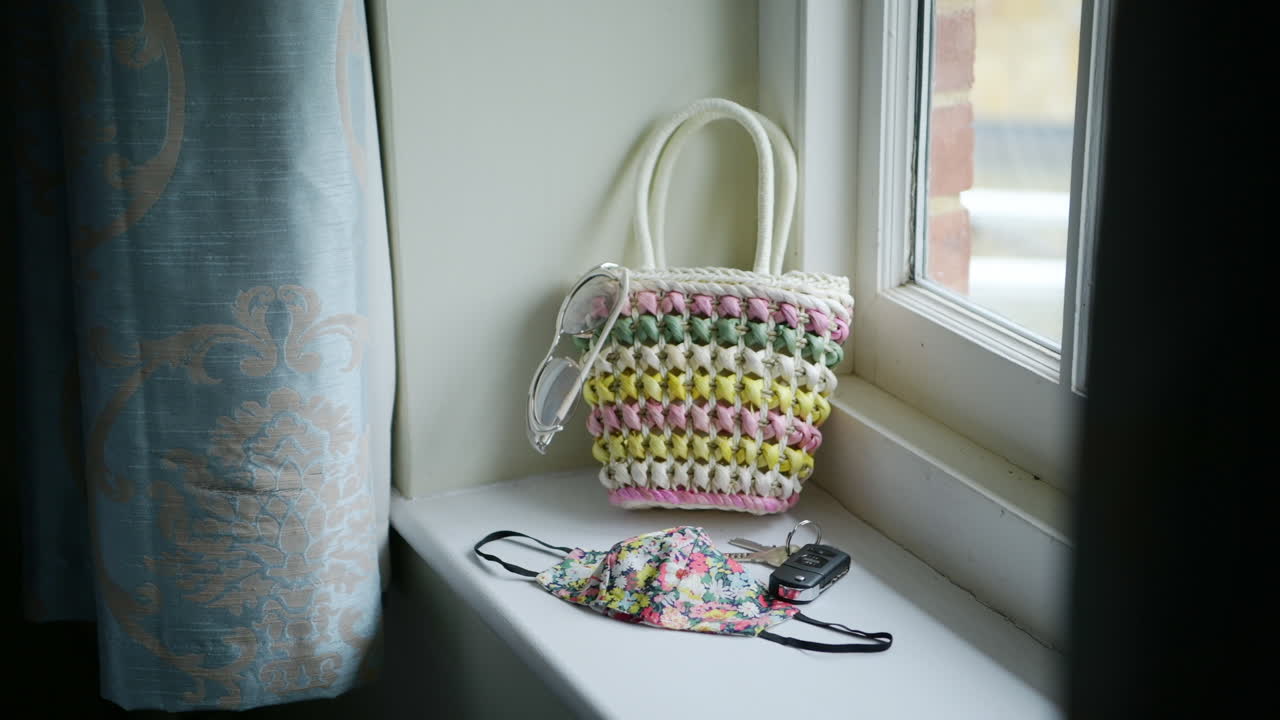 Woman grabbing cute bag and puts items in to leave house, face mask with flower pattern, sunny window frame, static shot
