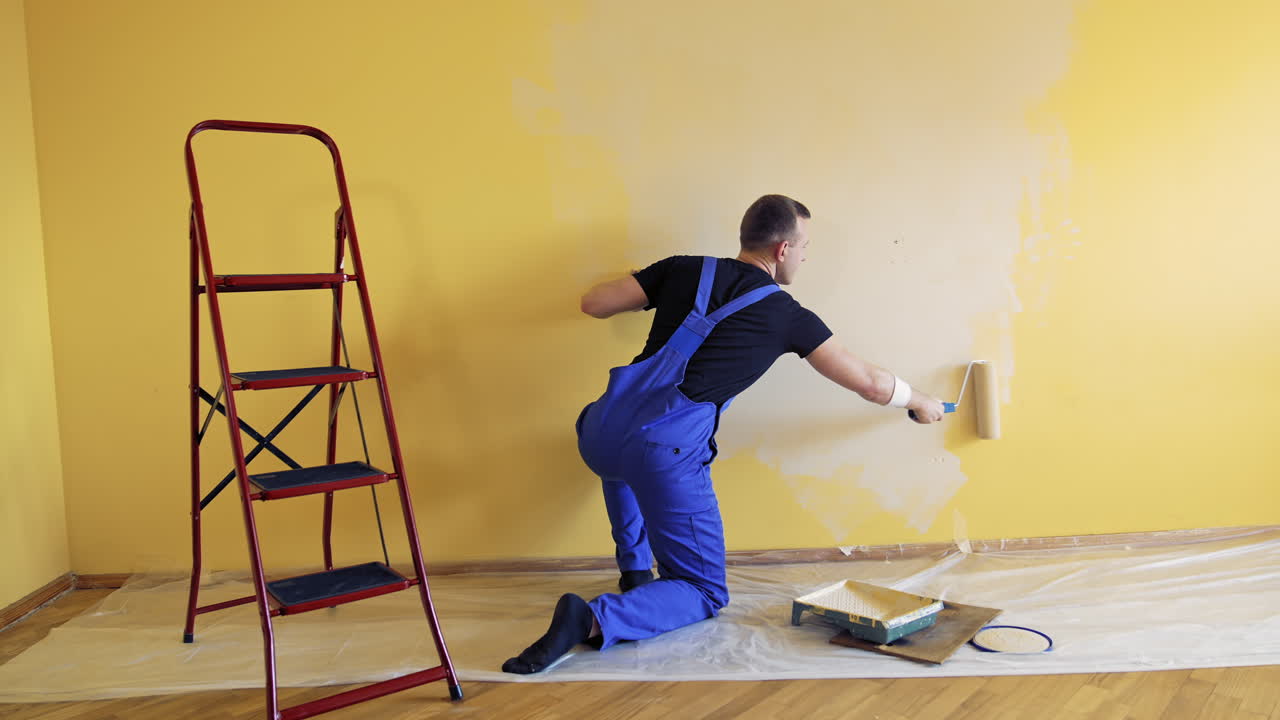 Young worker painting wall in room. Repair, building and home concept.