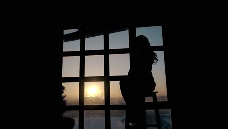 Silhouette-Einer-Traurigen-Dame,-Die-In-Der-Dämmerung-Am-Großen-Fenster-Sitzt