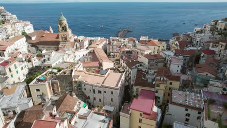 an aerial shot pushing towards the port of amalfi looking over the rustic slate roofs of historic amalfi town, one of the most popular tourist destinations on the world famous amalfi coast in italy