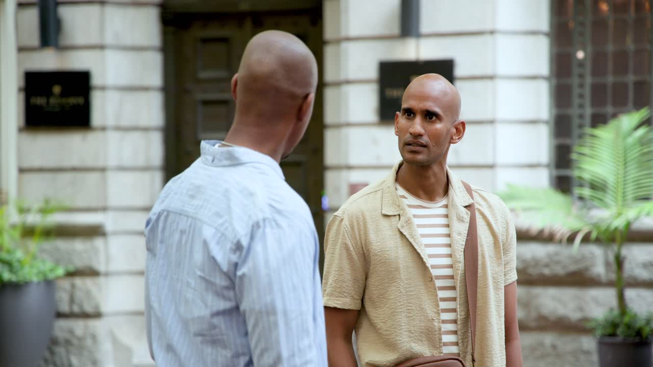 Homens afro-americanos iniciando conversa na calçada da cidade, o orador ajustando a bolsa transversal e explicando.