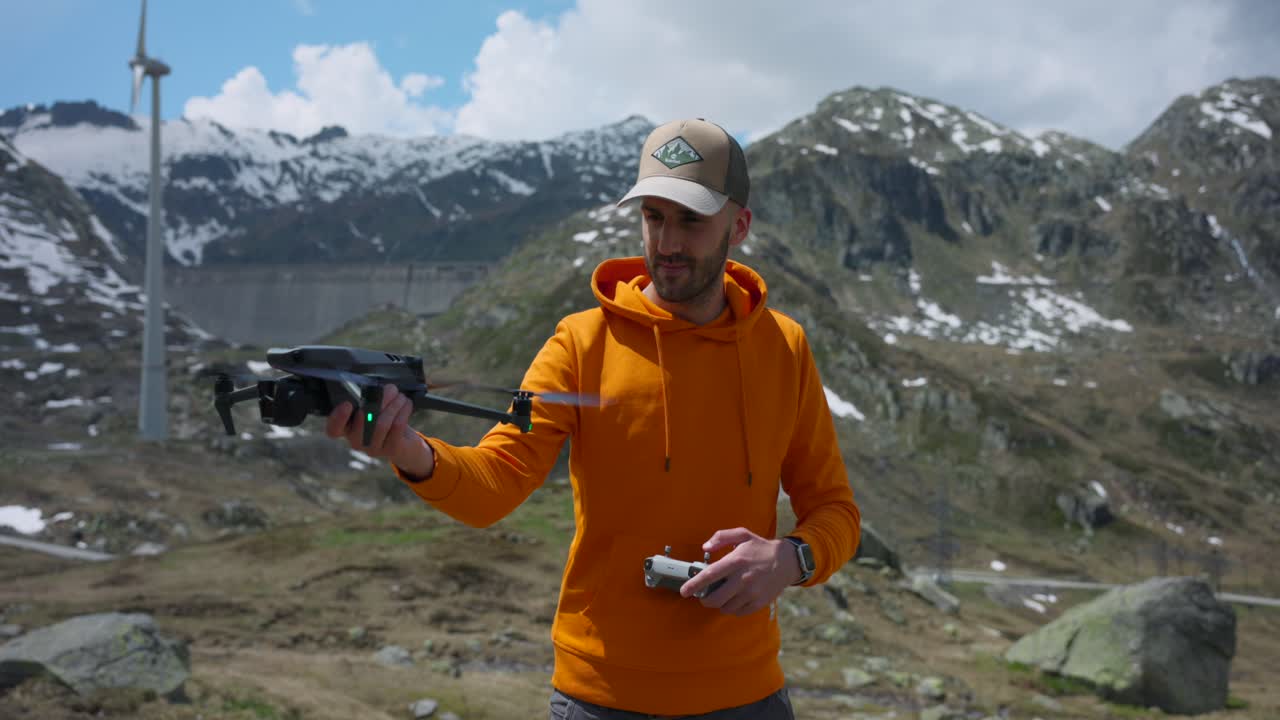 스위스 산 고타르도 근처 하늘에 손으로 드론을 발사하는 오렌지색 후디와 야구 모자를 입은 성인 남성
