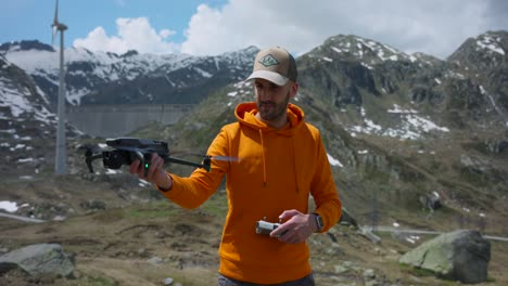 hombre adulto con capucha naranja y gorra de béisbol lanzando un avión no tripulado de la mano al cielo cerca de san gottardo, suiza