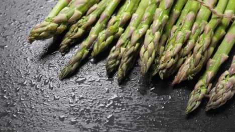 raw green asparagus on wet black slate background