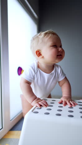 sweet little baby with adorable cheeks stands at the chair. kid looks up and walks around the stool. vertical video.