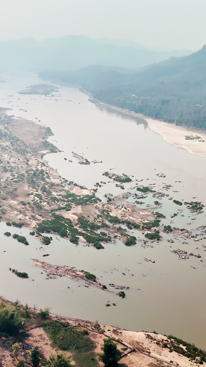 Vista aerea con drone del fiume Mekong che scorre attraverso montagne e foreste in Laos, con banchi di sabbia e isole visibili nell'ampio letto del fiume. Verticale
