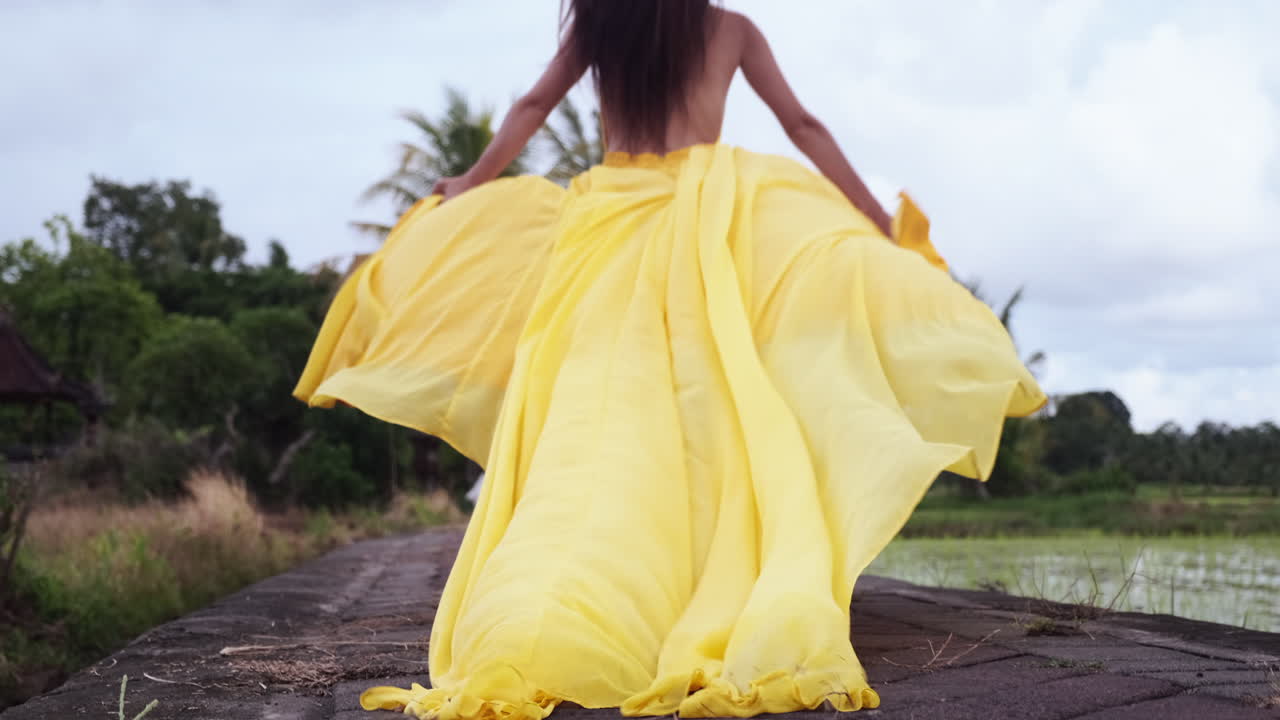 женщина в желтом платье идет по рисовому полю.