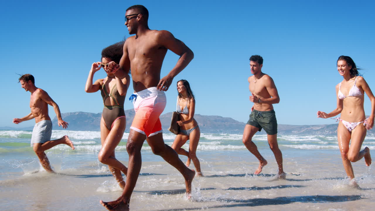 Gruppo di amici che corrono tra le onde in vacanza al mare
