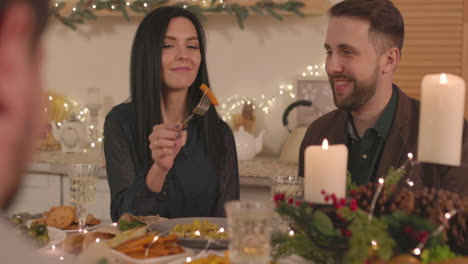 mujer sonriente alimentando a su novio con papas fritas durante la cena de navidad