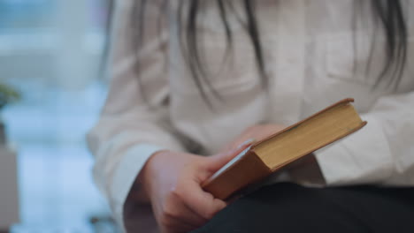 close up of elegant woman in white shirt holding book tightly as she angrily closes it, showing frustration. focus on hands and hardcover book, with blurred background