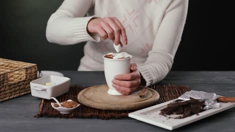 hands putting marshmallows into a cup of hot chocolate