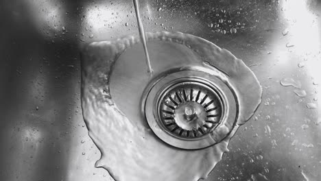 close up view from above of water pouring into a stainless steel sink