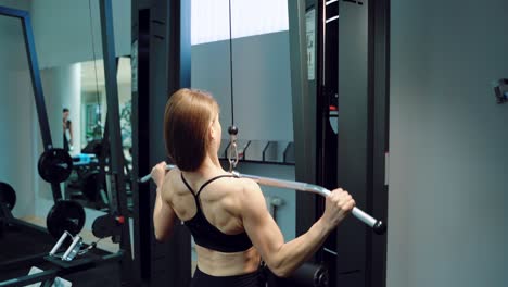 a strong woman in black top is doing vertical traction in the training in the fitness club. close-up