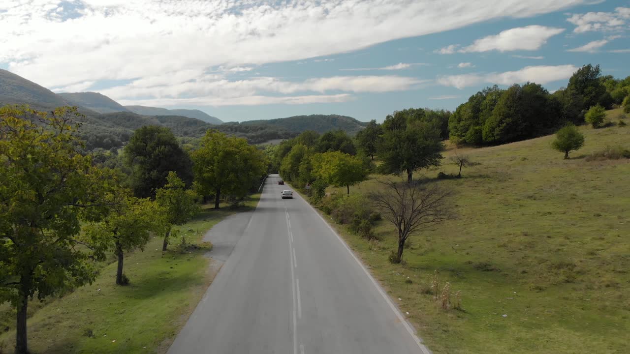 Tomada aérea de drone sobre estrada extraurbana e carros descendo a colina