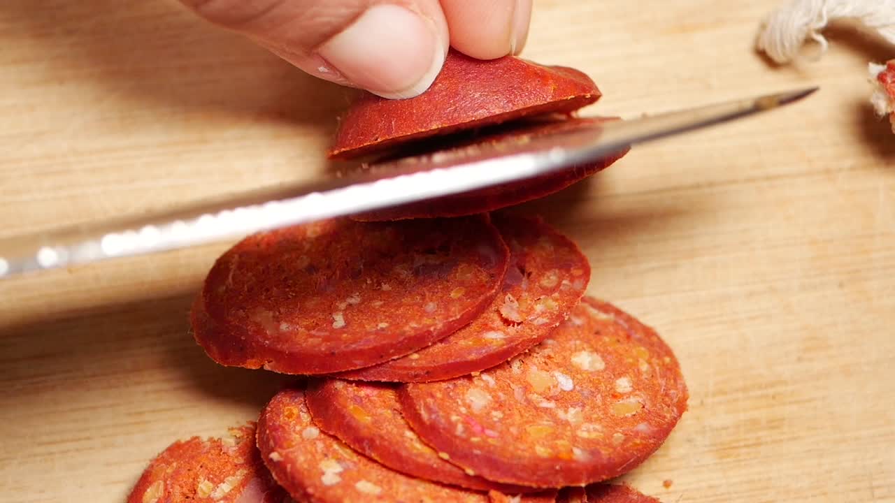 Hand schneidet rote Chorizo-Wurst auf einem Holzschneidebrett