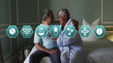 múltiples iconos médicos contra una pareja de ancianos afroamericanos riendo mientras están sentados en la cama