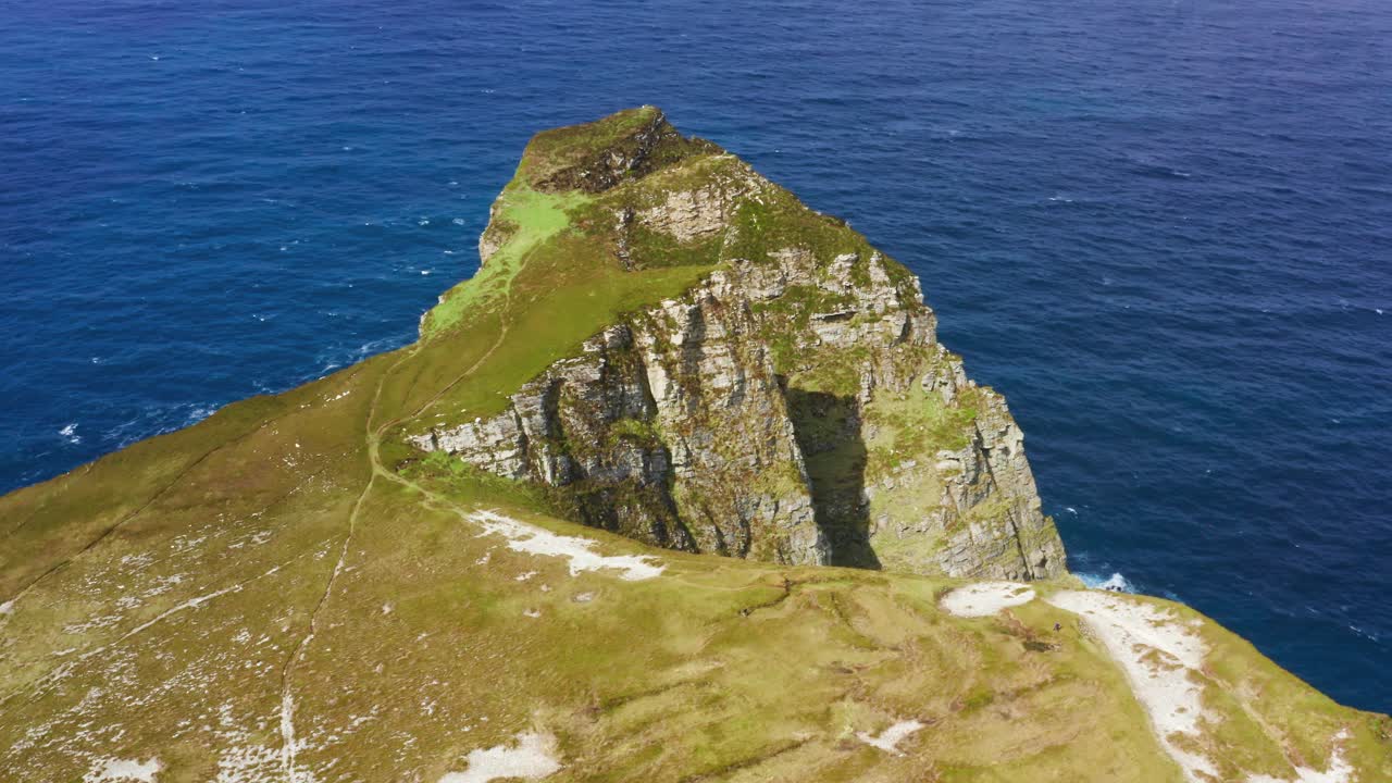 Orbiting aerial view of hikers walking the green clifftop of Horn Head with ocean in the background