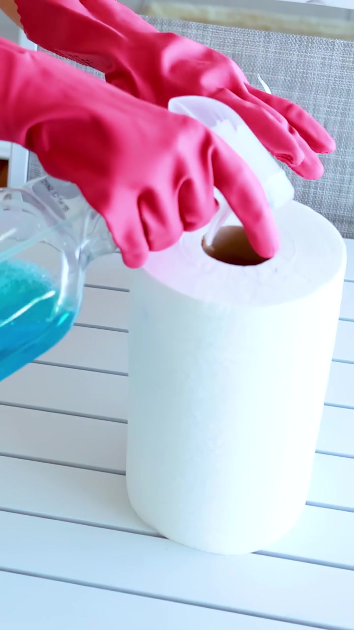 Mani con guanti rosa che spruzzano soluzione detergente su carta assorbente