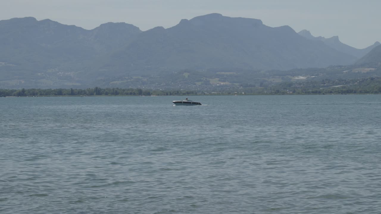 멀리 있는 배가 배경에 산과 구름이 가득한 도시와 함께 파란 물을 항해합니다.