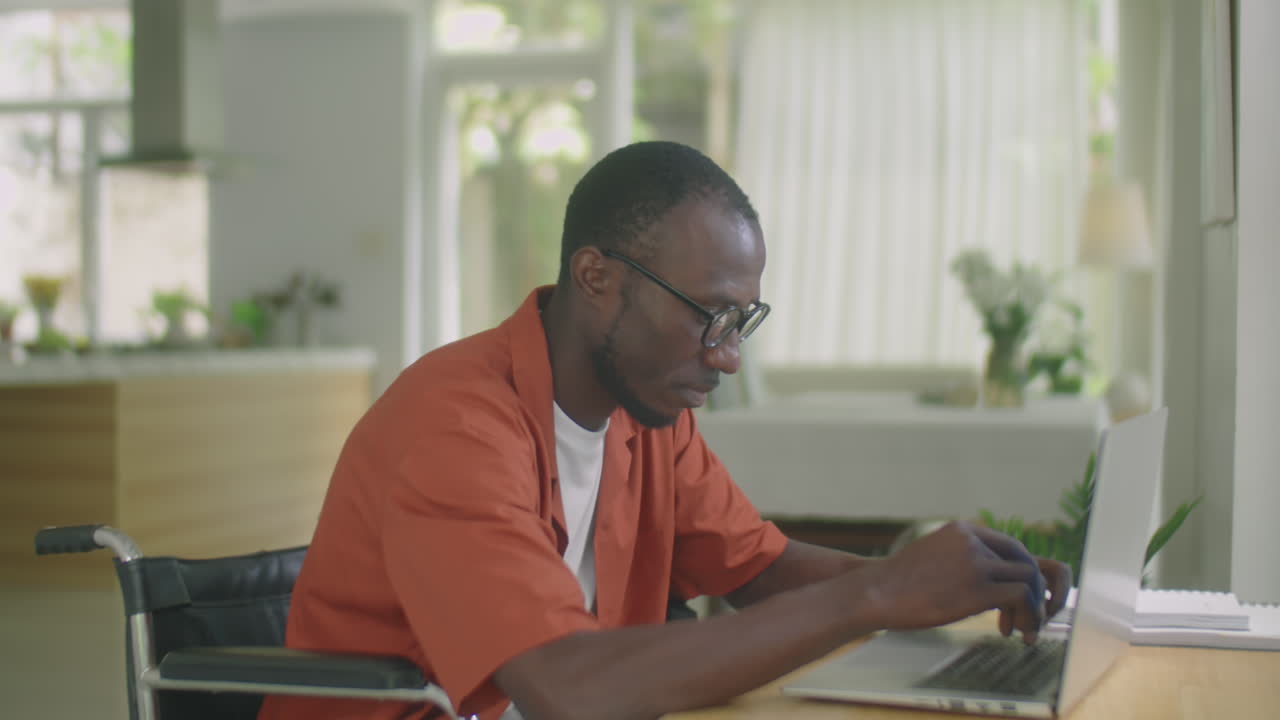 Uomo afroamericano su sedia a rotelle che digita al laptop