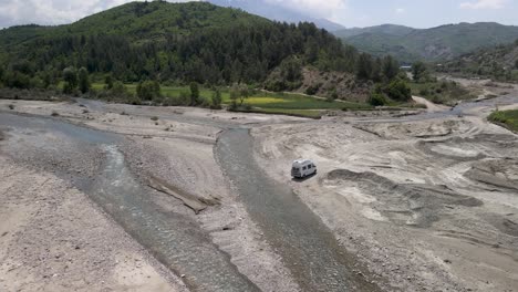 Camper-driving-on-unpaved-gravel-road-on-dry-streambed