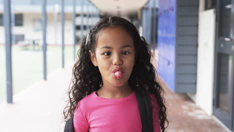 in a school corridor, a young african american girl sticks out her tongue