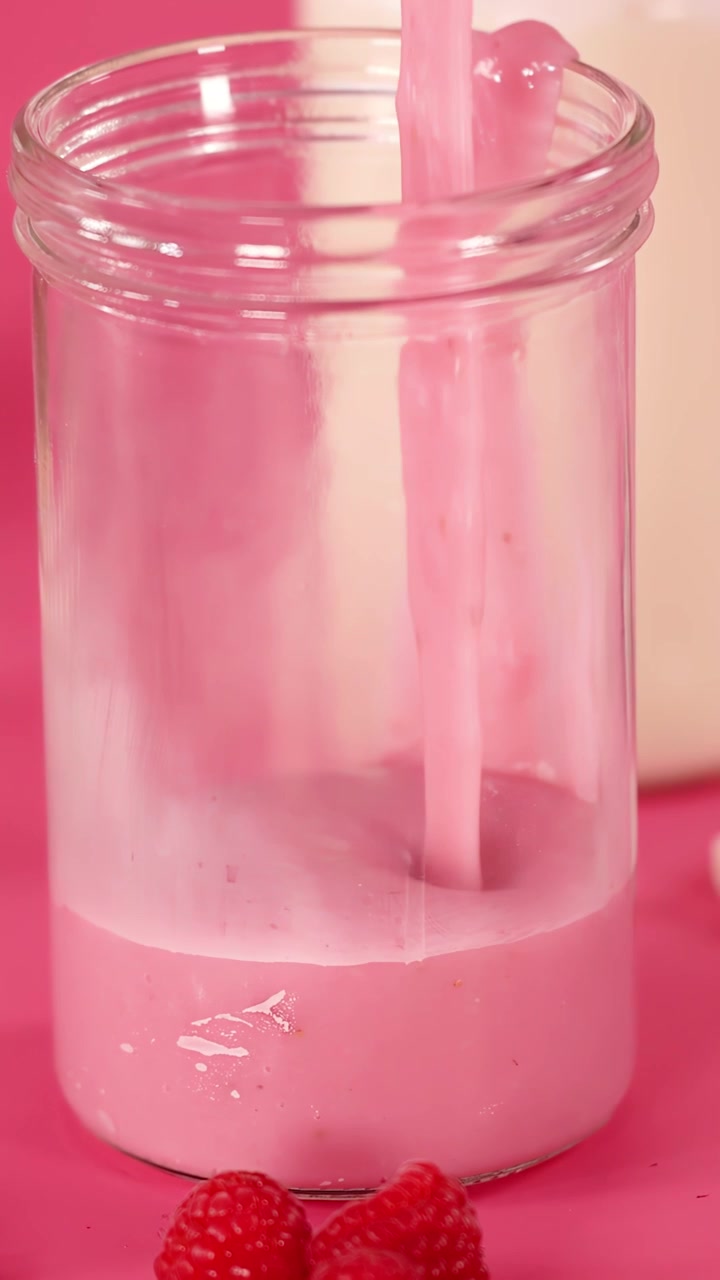Denso milkshake alla fragola si versa in un barattolo trasparente, sfondo rosa vibrante, illuminazione brillante, telecamera statica.