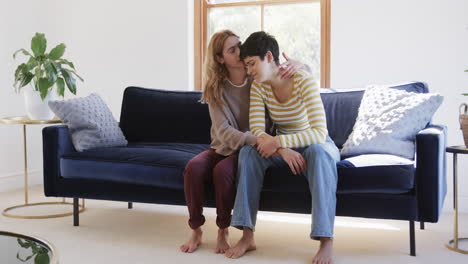 happy caucasian lesbian couple sitting on sofa, embracing and supporting each other in sunny house