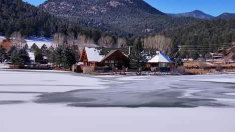 first snow ice frozen covered white evergreen lake house rocky mountain landscape scene morning front range denver aerial cinematic drone christmas ice skating hockey blue sky pan up forward motion