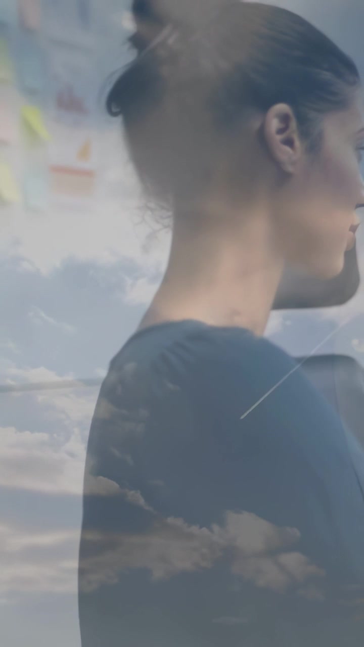 Mujer de oficina de pie girando la cabeza a la derecha, con nubes en el cristal creando una superposición mientras lee notas.