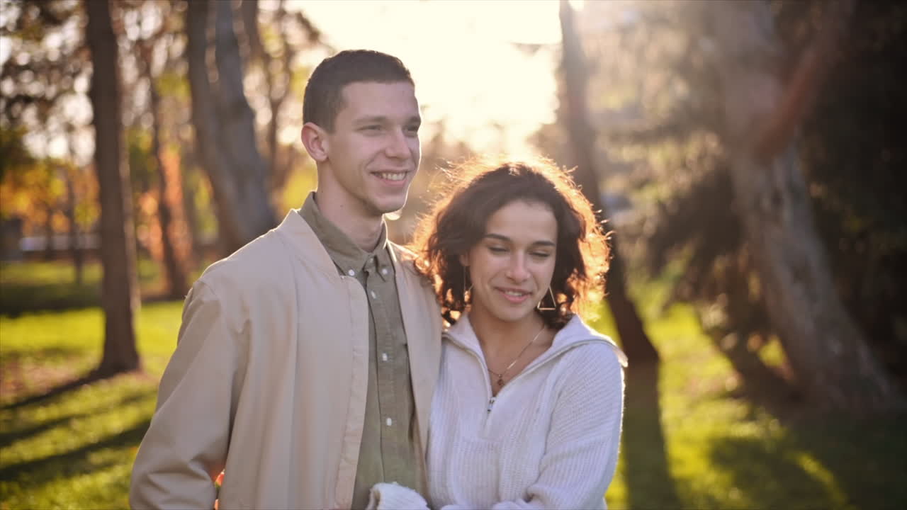 A romantic couple in an autumn park. Walking along the path hugging each other. Autumn atmosphere, yellowed trees and leaves around. Slow motion