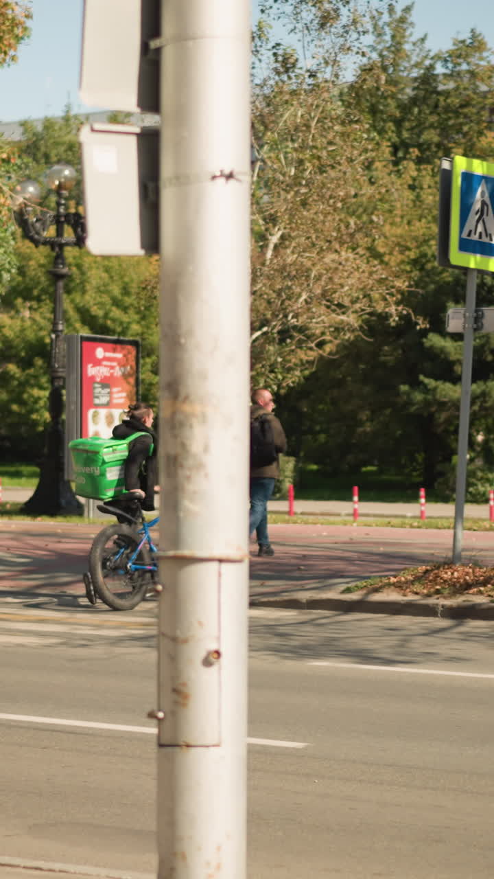 paso de peatones paso de cebra urbano cerca del parque peatón con mochila cruza el paso de cebra señalizado mientras un ciclista con bicicleta se detiene junto a una farola y una señal de carretera follaje otoñal diurno calma