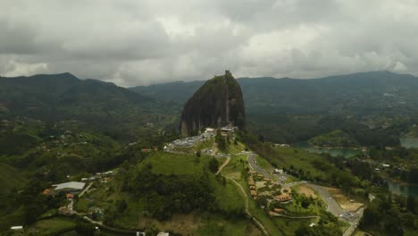 drone flies away from guatape rock revealing lakes and farmland below