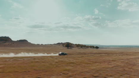 Seguimiento-De-Un-Disparo-De-Drone-De-Un-Coche-Negro-Conduciendo-A-Alta-Velocidad-Por-Una-Carretera-Rural-Al-Atardecer,-Camino-Polvoriento,-Grado-Cinematográfico