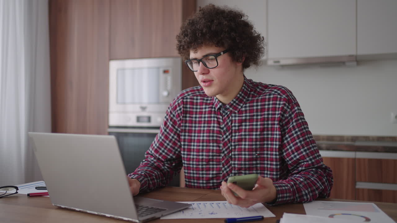Young man with smartphone in his hands. Modern businessman or student at home office. Freelancer at work. Young student man study at home with laptop and uses a smartphone