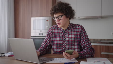 young man with smartphone in his hands. modern businessman or student at home office. freelancer at work. young student man study at home with laptop and uses a smartphone